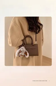 Brown vintage handbag with grey plush rabbit charm worn by a model in a camel coat