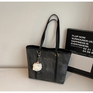 Detail of dark gray tote bag with stone texture, gold slogan, and white plush lamb charm
