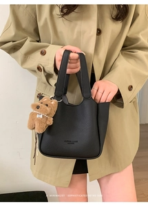 Detail of black pebbled leather bucket bag with cute plush bear charm on handle
