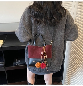 Detail of burgundy suede and black leather patchwork bucket bag with pom-pom charm
