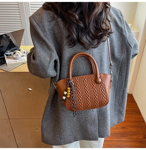 Detail der braunen geflochtenen Eimertasche mit dekorativer Perlenquaste und stabilem Griff