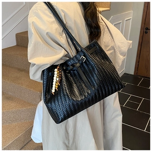 Détail d'un sac cabas tressé noir avec motif à chevrons et breloque en perles sur un mannequin