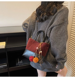 Detail view of burgundy and black bucket bag with fur balls and beaded tassels