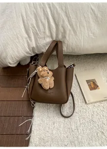 Detail of dark brown lychee leather bucket bag with cute plush teddy bear charm