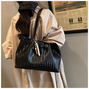 Détail du cabas tressé noir avec lanières en cuir et breloque vintage en perles de bois