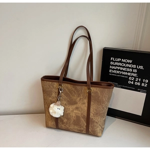 Close-up of vintage brown tote bag with marble texture and white plush charm on white surface