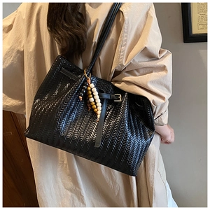 Detail of black woven tote bag featuring beaded fringe tassel and side metal buckle design