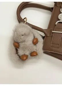 Detail of a fluffy grey rabbit charm with gold buckle on a brown leather handbag