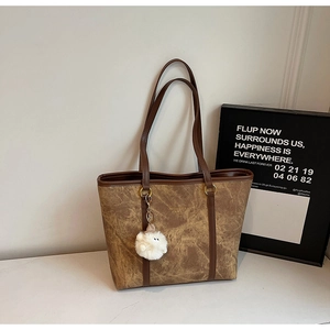 Close-up of brown textured tote bag with metal rings and white plush sheep keychain