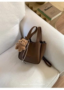 Detailed view of a brown pebbled leather bucket bag with plush bear charm on a sofa
