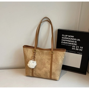 Detail view of tote bag with marble texture, brown leather handles and plush charm