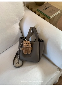 Detail of leather bucket bag with plush charm and gold logo on white sofa