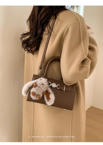 Retro brown leather crossbody bag detail with cute bunny charm on a model in a winter coat