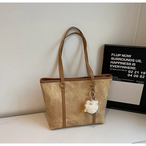 Detail of khaki tote bag with matte texture, long straps and cute plush pendant charm