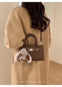 Detail of dark brown leather crossbody bag with silver hardware and plush rabbit charm
