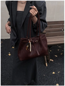 Détail d'un grand sac cabas bordeaux tissé avec pendentif perlé en scène extérieure