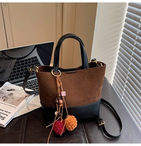 Detail view of a vintage two-tone bucket bag with plush charm on a leather desk