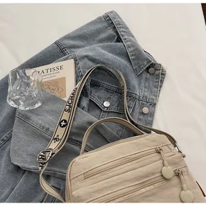 Detail of wide woven strap and multi-layer zipper pockets on beige crossbody bag