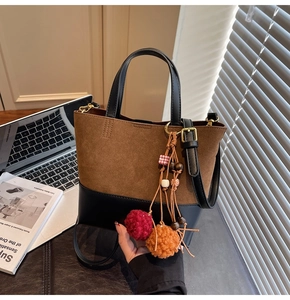 Detail of brown suede tote bag featuring colorful pompom tassels and black leather handles