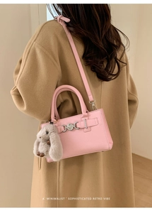Pink pebbled leather crossbody bag with rabbit charm worn with a beige wool coat