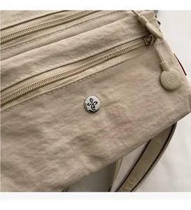 Detail of multi-layer zipper compartments and silver logo on nylon crossbody bag