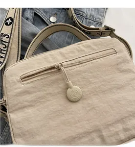 Close-up of beige nylon crossbody bag featuring smooth zipper detail and woven shoulder strap