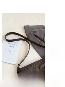 Detail of dark brown leather shoulder bag with pebbled texture and metal logo plaque