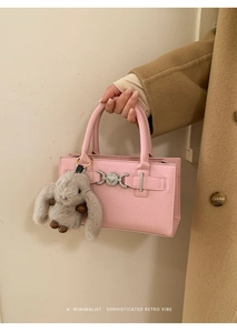 Detailed shot of pink textured leather handbag with heart buckle and rabbit charm on coat