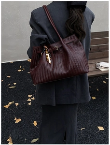 Détail du sac cabas tissé bordeaux avec breloque en bois sur un fond automnal gris