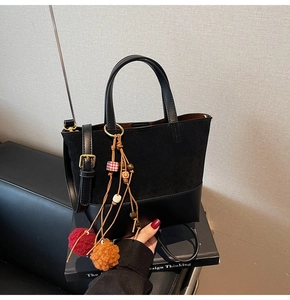 Close-up of black bucket bag with mixed textures, golden buckles and pom-pom charm