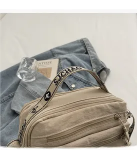 Detail view of beige nylon crossbody bag featuring multiple zipper pockets and wide handles