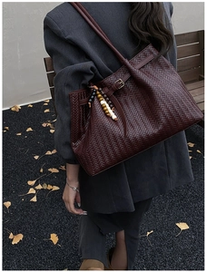 Outdoor shot of a woven burgundy tote bag with unique ethnic wood bead decoration
