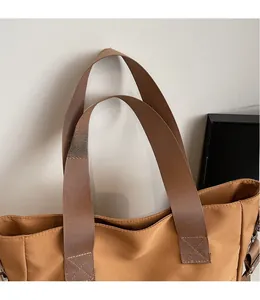 Detail of reinforced cross-stitching on brown canvas tote bag with wide nylon strap
