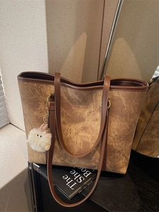 Brown vintage textured tote bag with dark leather straps and plush charm on table