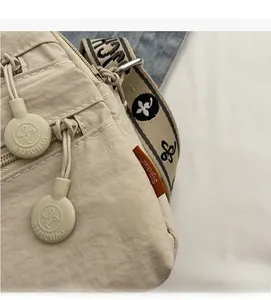 Detail of beige nylon crossbody bag featuring branded logo zipper and leather label