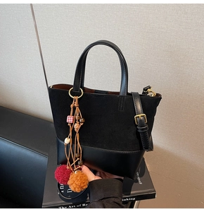 Detail of vintage black bucket bag showing suede stitching and colorful pompom charm