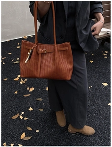 Close-up of brown woven tote bag with buckle detail and beaded charm in autumn setting