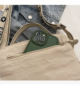 Detail of front zipper pocket on beige nylon crossbody bag holding a smartphone