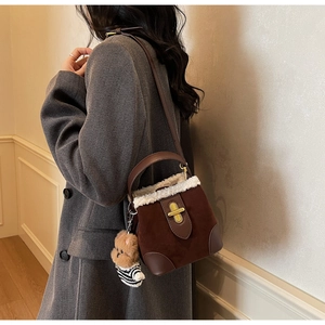 Detail of faux shearling trim and cute bear charm on a brown suede crossbody bucket bag