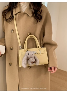 Detail of yellow lychee leather handbag with plush bunny charm and metal buckle
