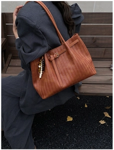 Detailed view of brown woven PU leather tote bag with retro bead charm on a wooden bench