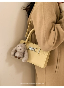 Detailed side view of cream yellow textured leather crossbody bag with rabbit charm