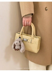 Detail of yellow pebbled leather crossbody bag with silver hardware and plush bunny charm