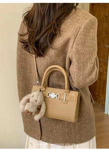 Detail of camel retro crossbody bag with heart buckle and plush bunny charm on coat