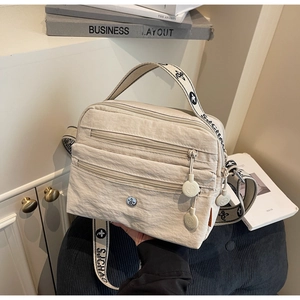 Detail of off-white pleated nylon crossbody bag showing multiple zip layers and wide strap