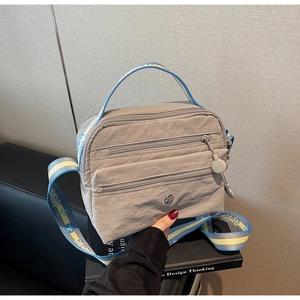 Detail view of grey crossbody bag with multi-zipper compartments and patterned strap