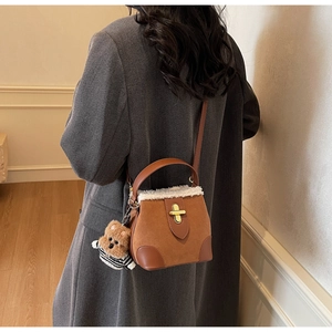 Detail of suede bucket bag with white faux fur trim, gold twist lock and a cute bear charm
