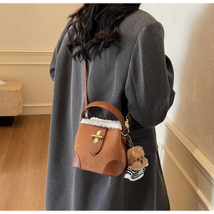Brown faux suede bucket bag with white fleece trim and cute bear charm worn by a model