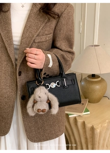 Close-up of black pebble leather handbag with silver clasp and plush rabbit charm