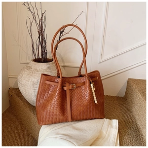 Détail du sac cabas marron en cuir tressé avec boucle décorative et breloque perlée